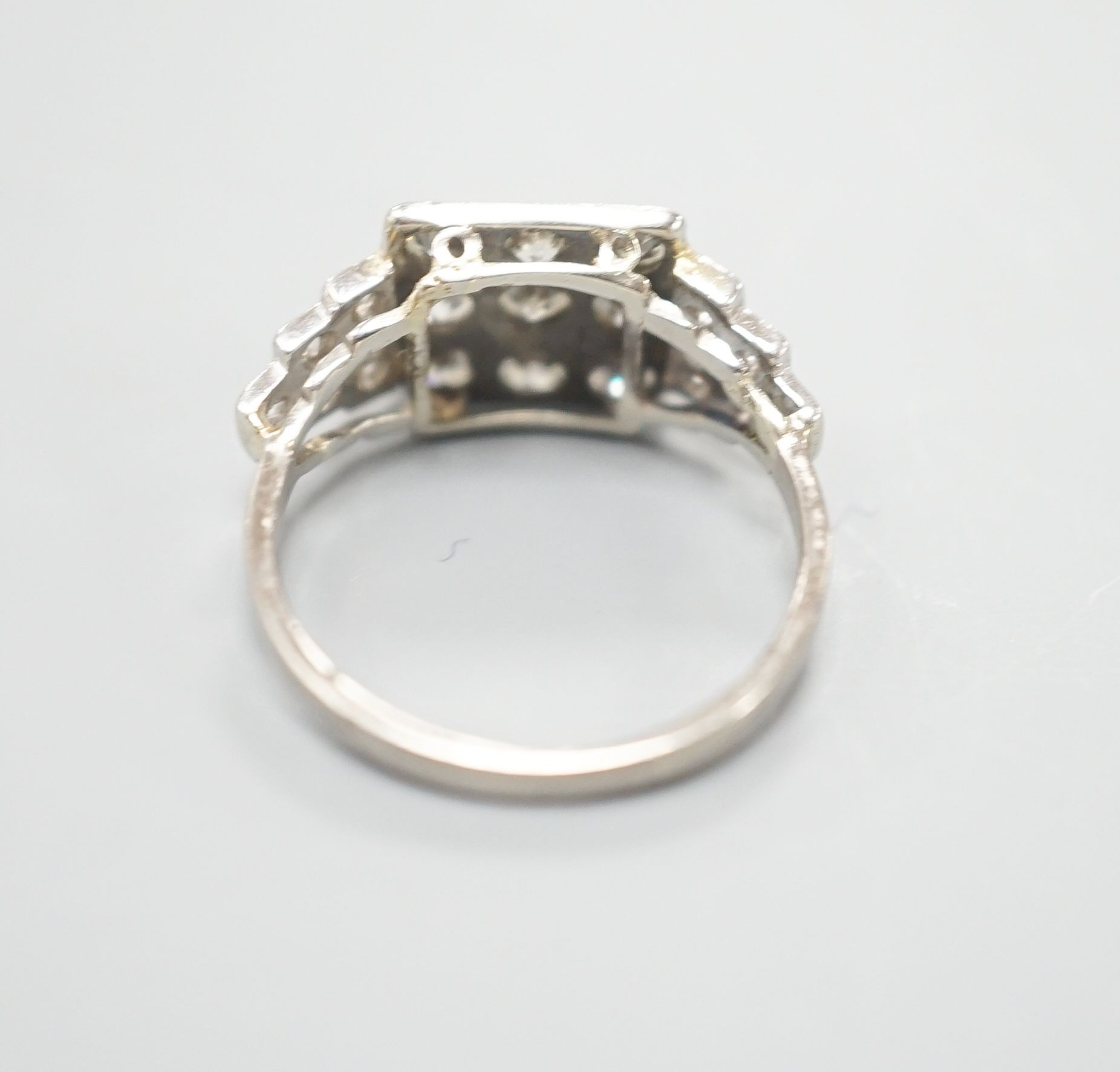 An Art Deco style white metal and nine stone diamond set tablet ring, with diamond set stepped shoulders, size K, gross weight 3.2 grams.